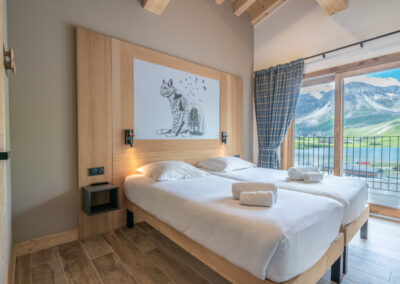 Une chambre avec deux lits et un balcon donnant sur les montagnes.